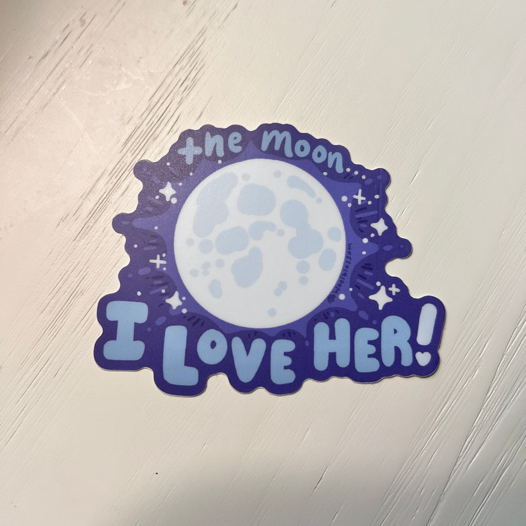 Sticker with moon design and 'I love her!' text on a light wooden surface