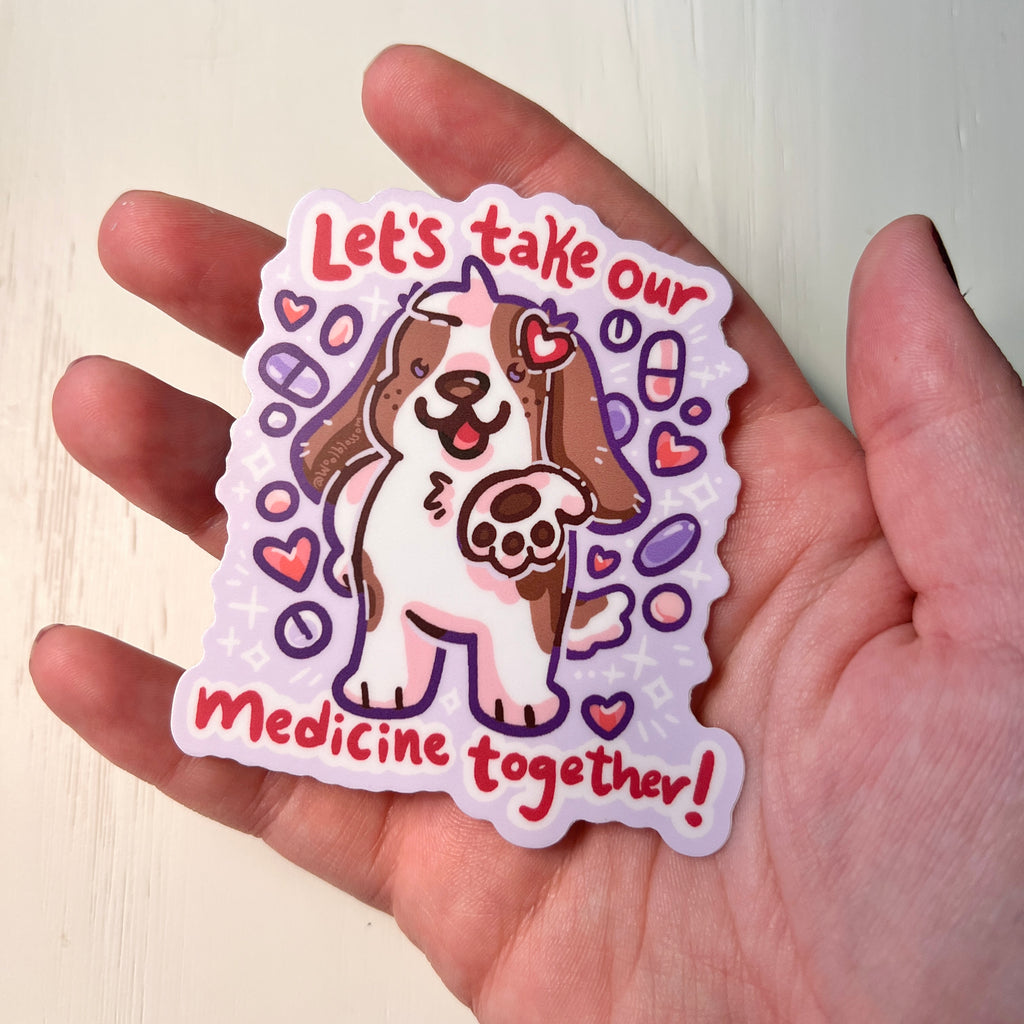 Sticker with a dog illustration and text 'Let's take our medicine together!' held in a hand.