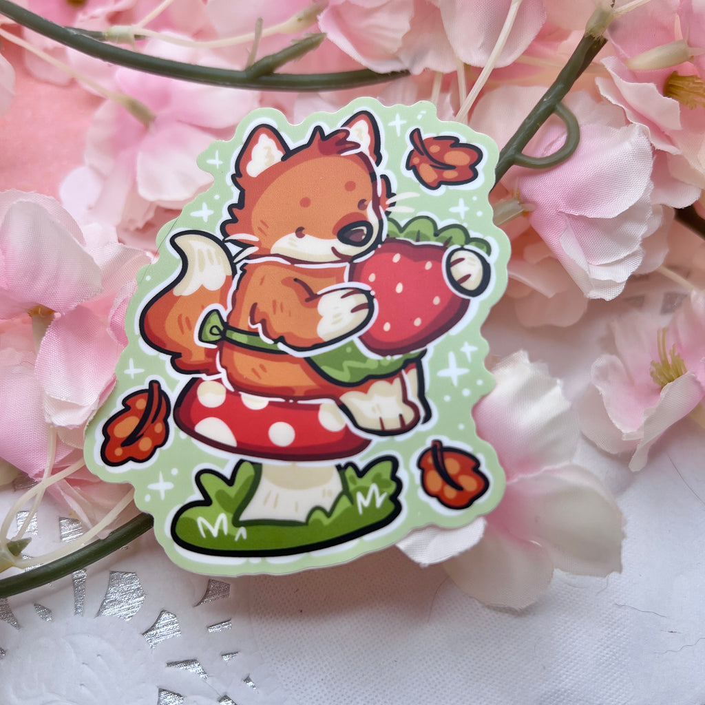 A sticker of a red fox with a little green apron sitting on a red mushroom, holding a strawberry with autumn leaves falling