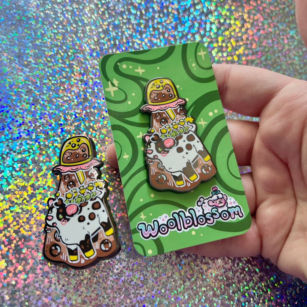 An alien boba cow being abducted by a boba enamel pin on a green card with 'Woolblossom' branding, on a glitter background