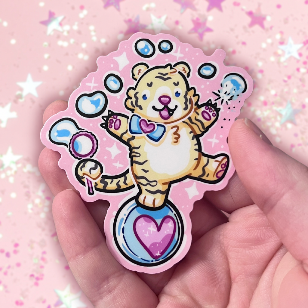 A sticker of a cute tiger balancing on a ball, bubble wand in tail, reaching up and poking the bubbles with his claws. Pink aesthetic overall.