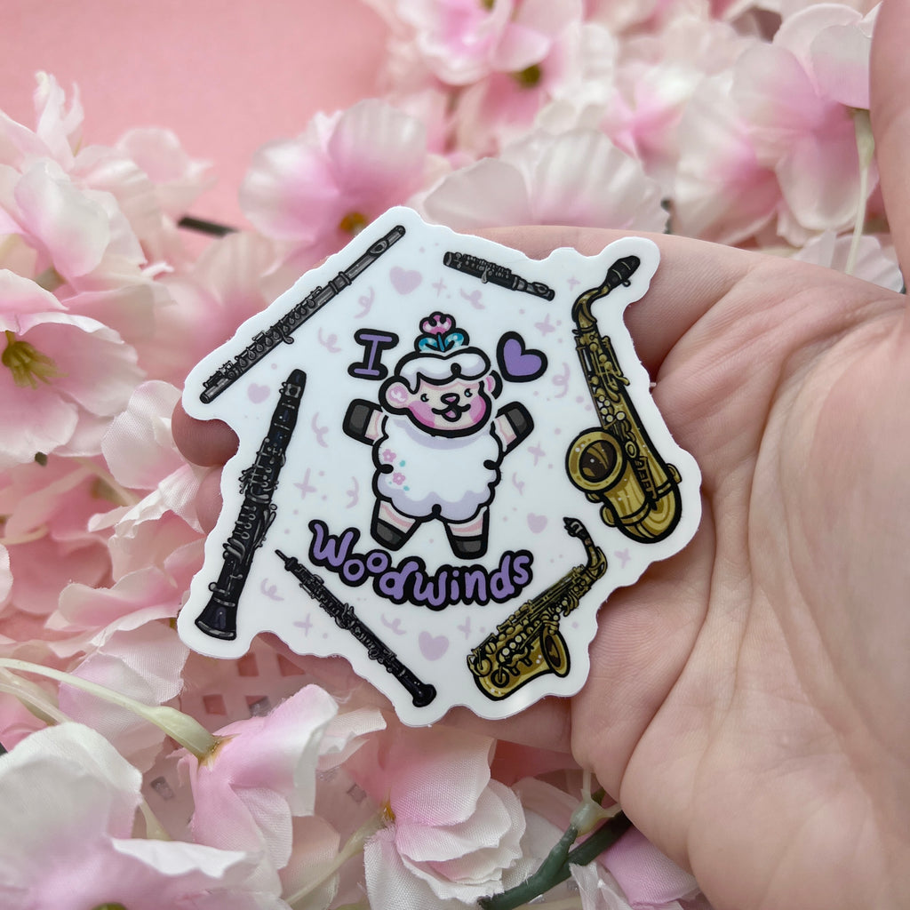 a sticker of a sheep with the text "I heart woodwinds" and six instruments floating around them (flute, piccolo, tenor sax, alto sax, oboe, clarinet)