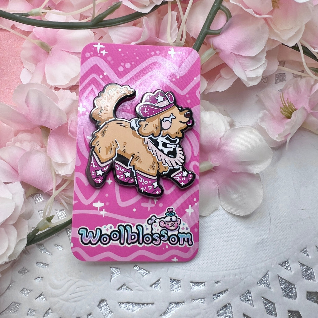 An enamel pin of a golden retriever happily stepping, dressed in a pink cowgirl hat, boots, and bandanna 