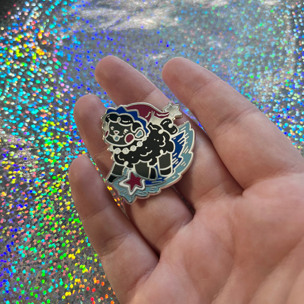 Hand holding the space witch sheep enamel pin against a glittery background