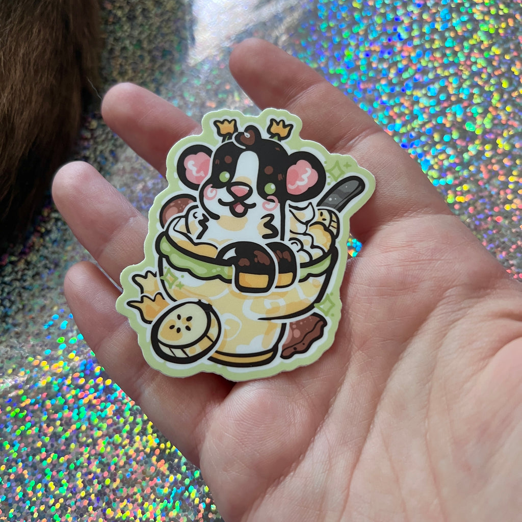 A sticker of a daffodil cow in banana pudding in a hand on glittery background