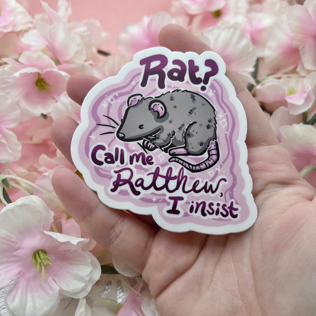 a sticker of a grey rat on a pink solid background with the text "Rat? Call Me Ratthew, I Insist"