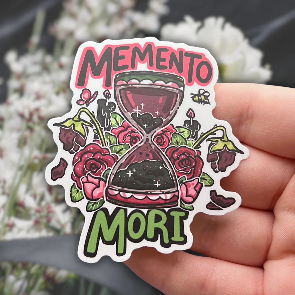 A sticker of a red and black hour glass surrounded by roses at various stages of their lifespan with text that says “memento mori”