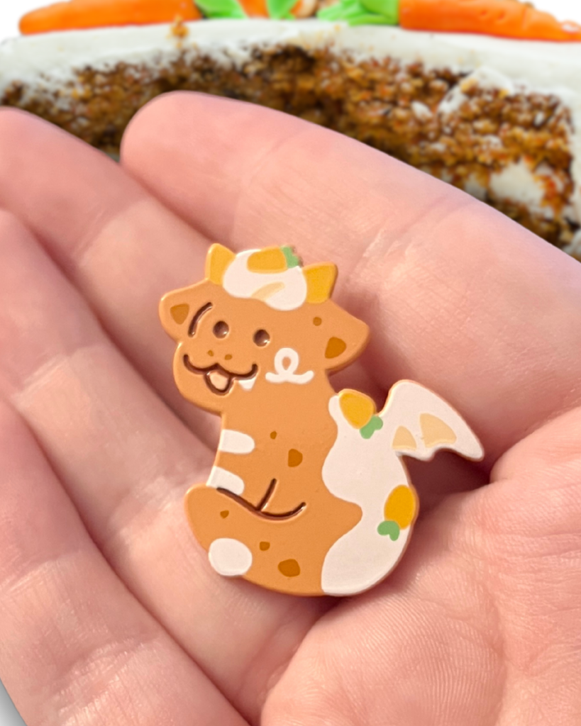 carrot cake dragon pin held in a hand