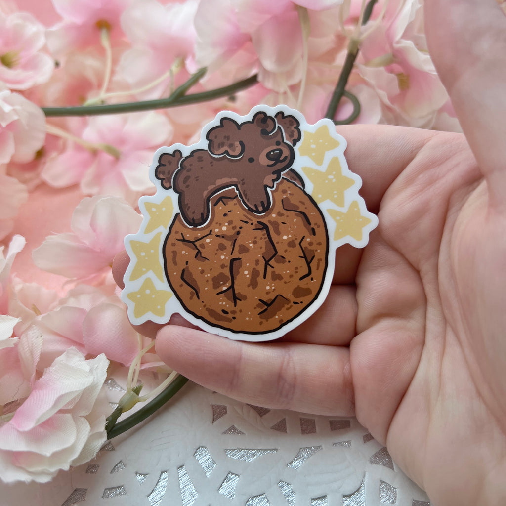 A sticker of a brown puppy on top of a ginger snap cookie with yellow stars