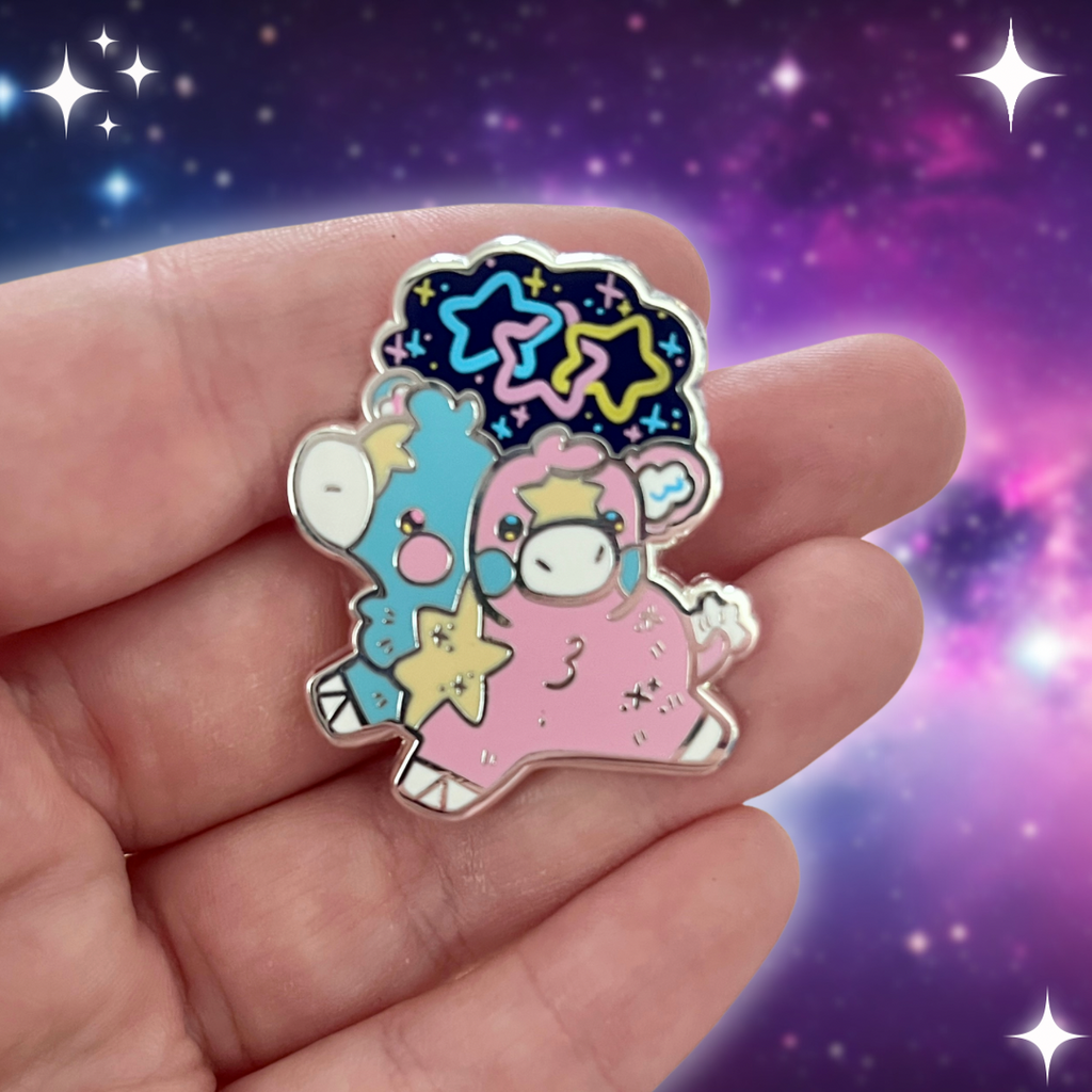 An enamel pin of a two headed calf, one is blue and one is pink, with a yellow star pattern connecting them and on each forehead. On top is a starry sky with three interlocking stars, one blue, one pink, and one yellow.