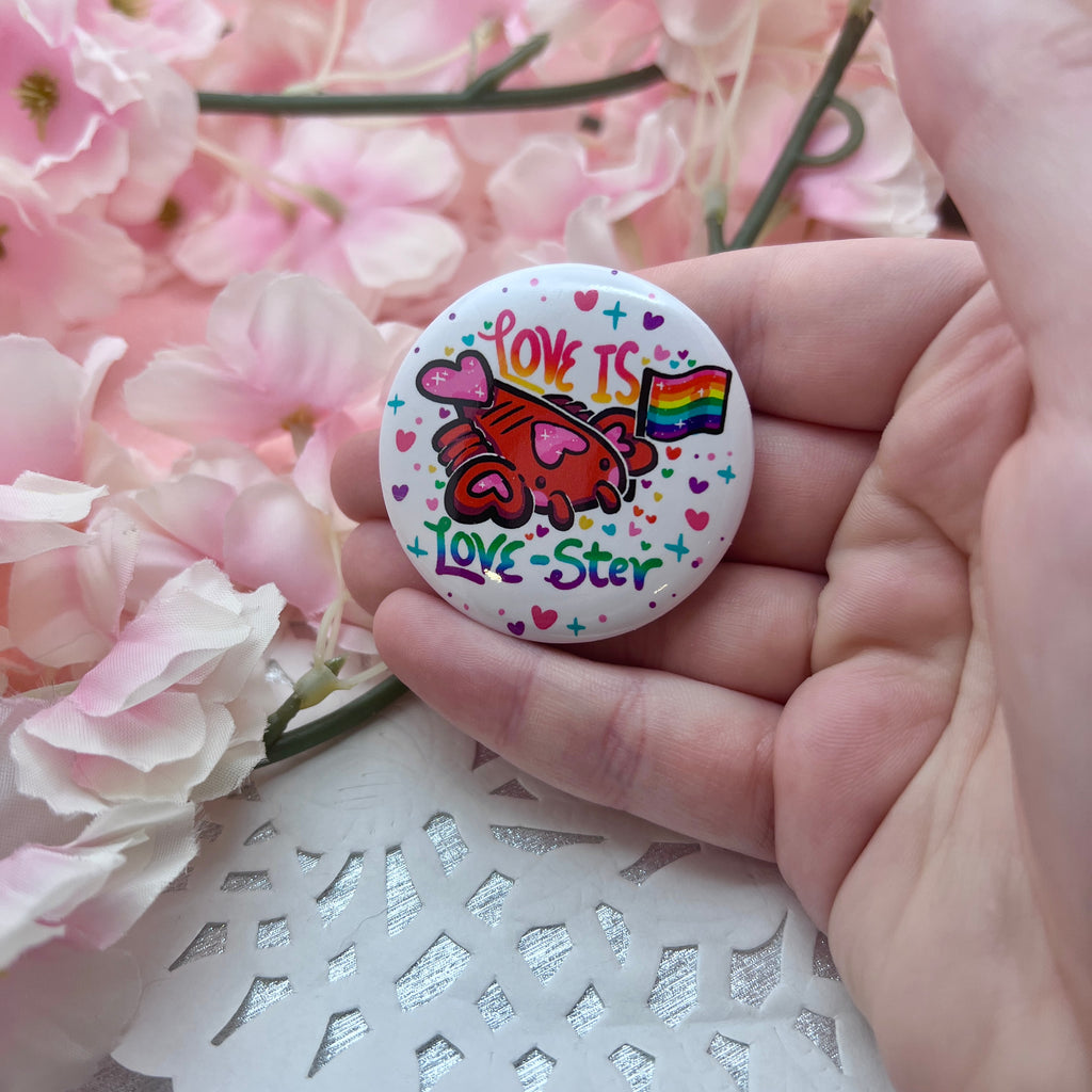 A button of a heart themed lobster holding a rainbow pride flag with text that says "love is love-ster"