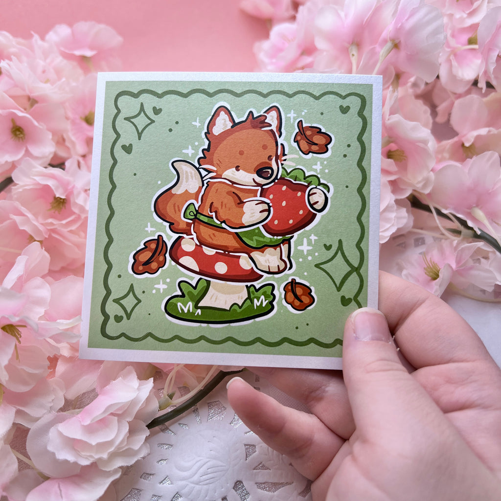 A print of a red fox with a little green apron sitting on a red mushroom, holding a strawberry with autumn leaves falling