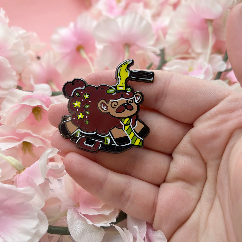 an enamel pin of brown sheep with a mustache and a tie laying on a suitcase, getting bonked on the head by a hammer