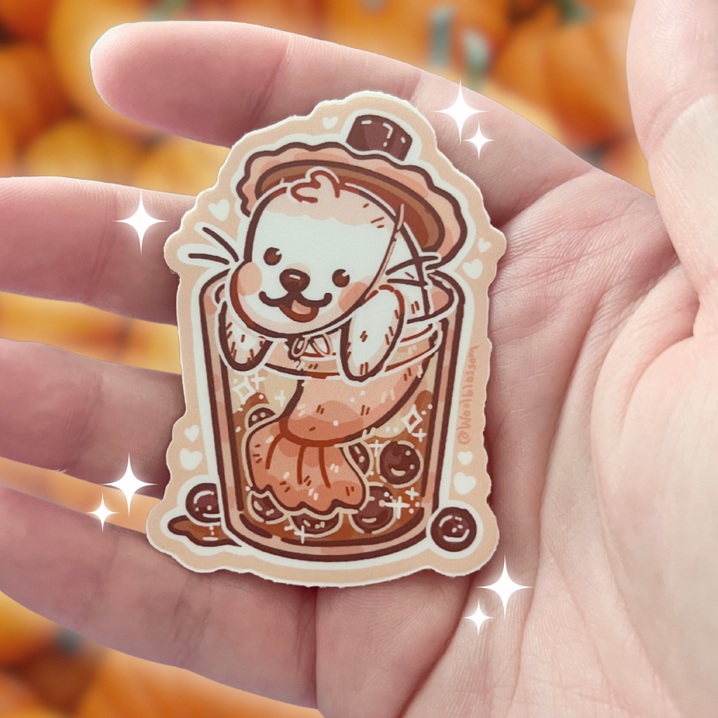 Sticker of a seal in a boba cup held in a hand with a blurred pumpkin background