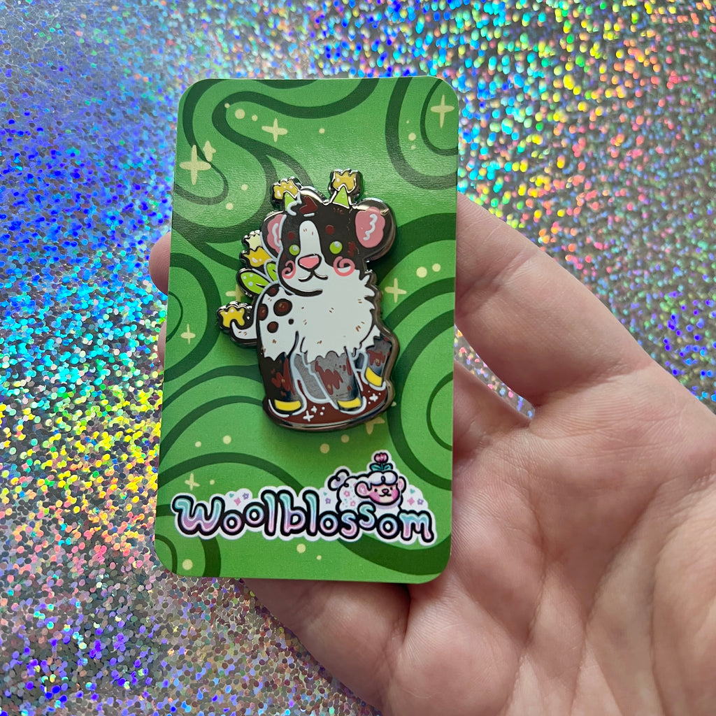 Same pin on a green card held by a hand against a glittery background