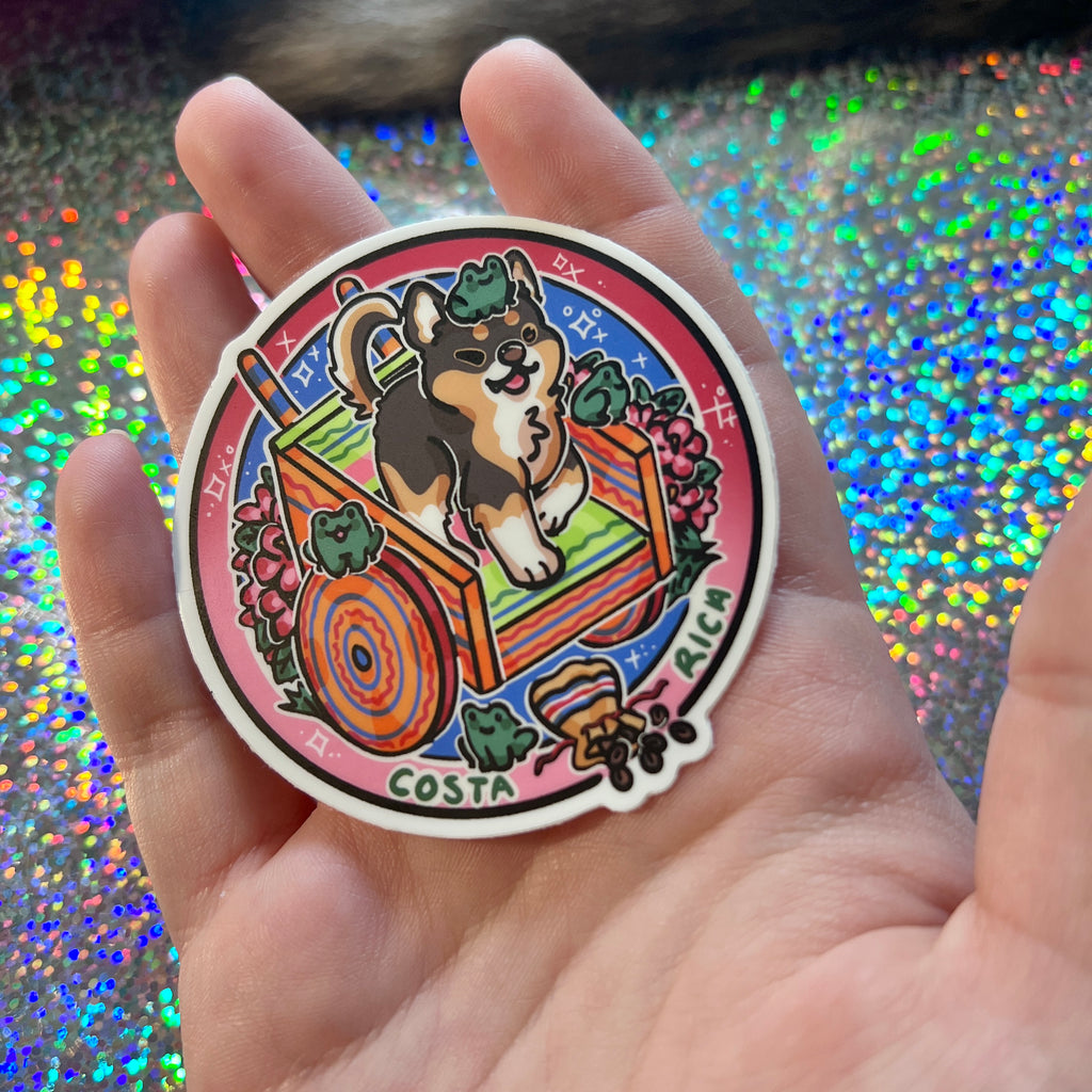 a sticker of a chihuahua on a decorative cart, surrounded by flowers, frogs, and chocolate on a glittery background