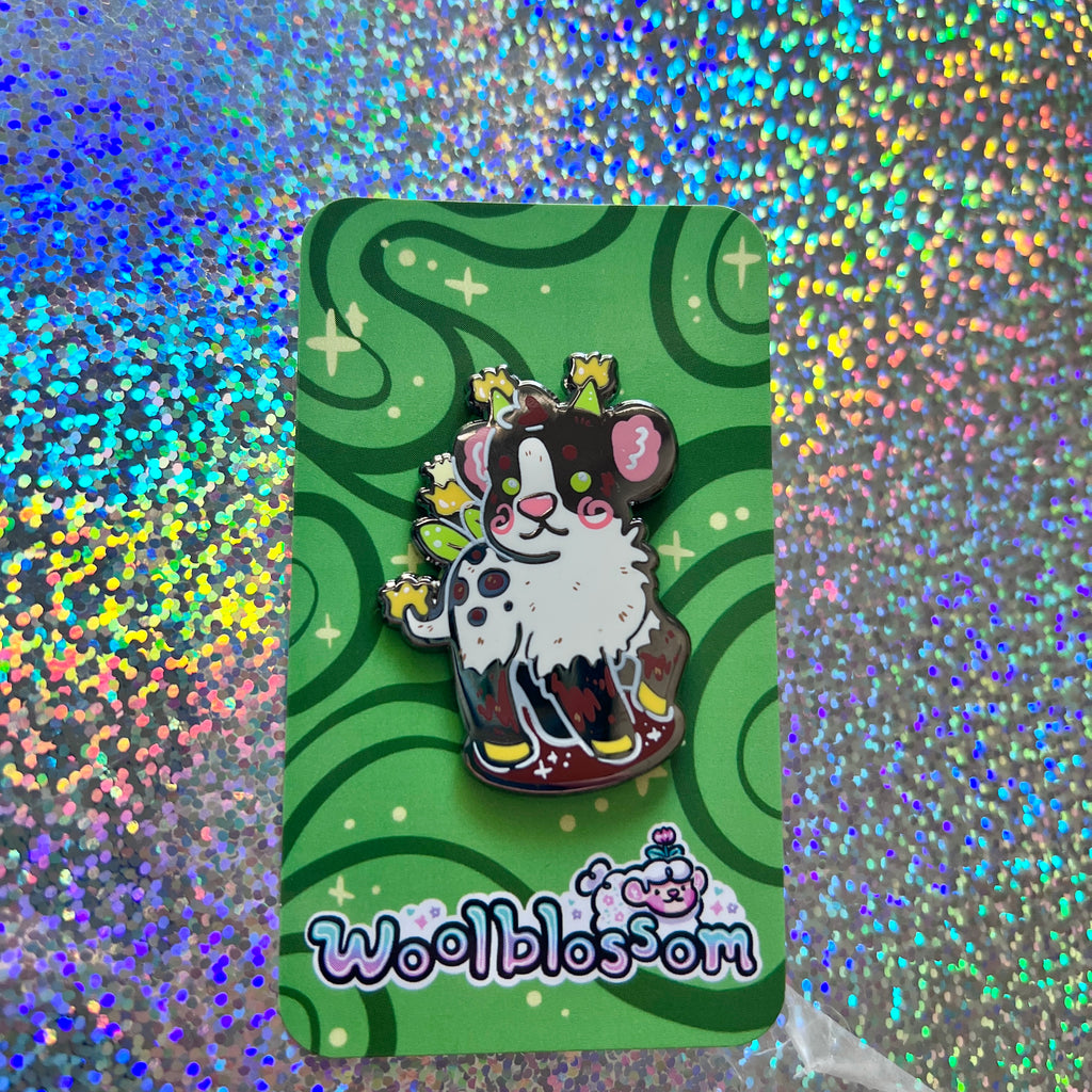 Same pin on a green card held by a hand against a glittery background