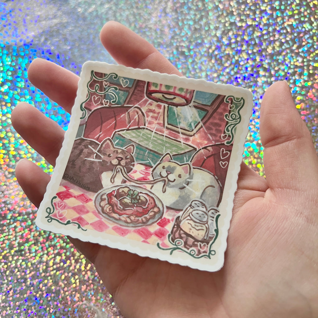 Hand holding a sticker of two cats eating spaghetti in a restaurant against a glittery background
