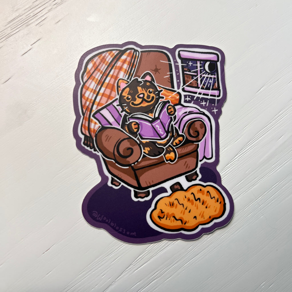 Sticker of a cat reading in a chair on a hand on a white background