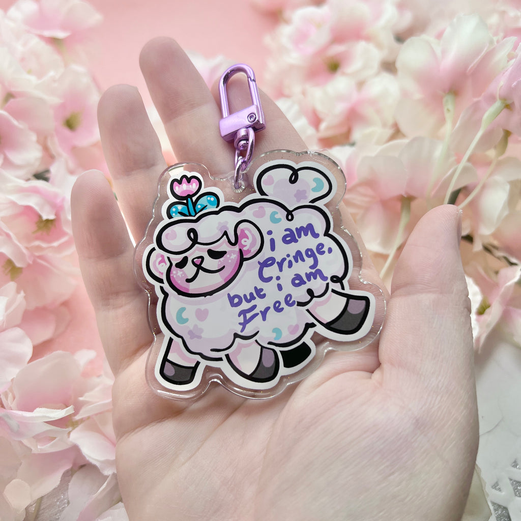 A keychain of sprout the flower sheep mid gallop, with purple text on their wool that says "i am cringe, but i am free"