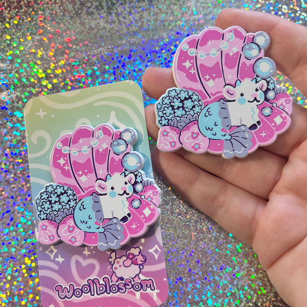 Enamel pin of a mermaid goat in a seashell on a glittery background