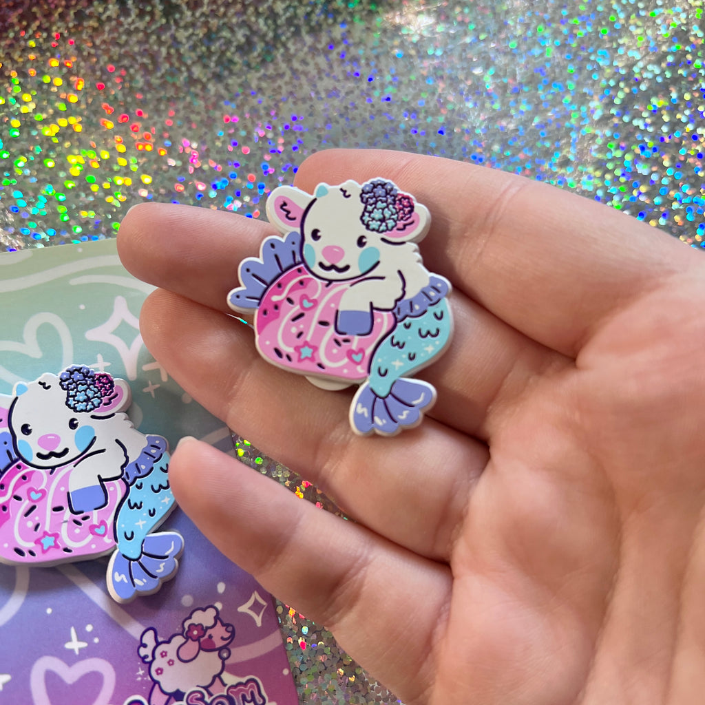 Hand holding a colorful mermaid-themed pin with a glittery background