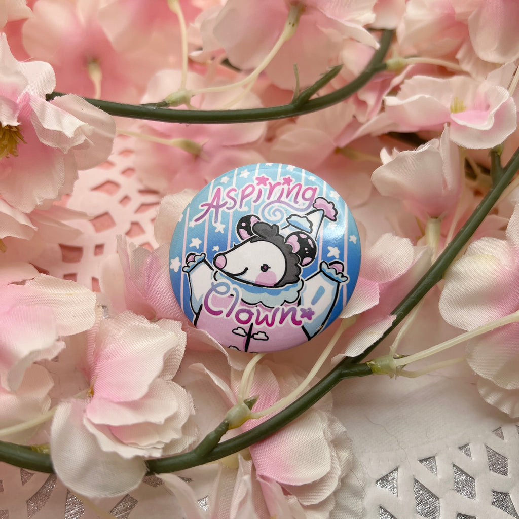 A button of a cloud themed opossum that looks happy with the text "aspiring clown"