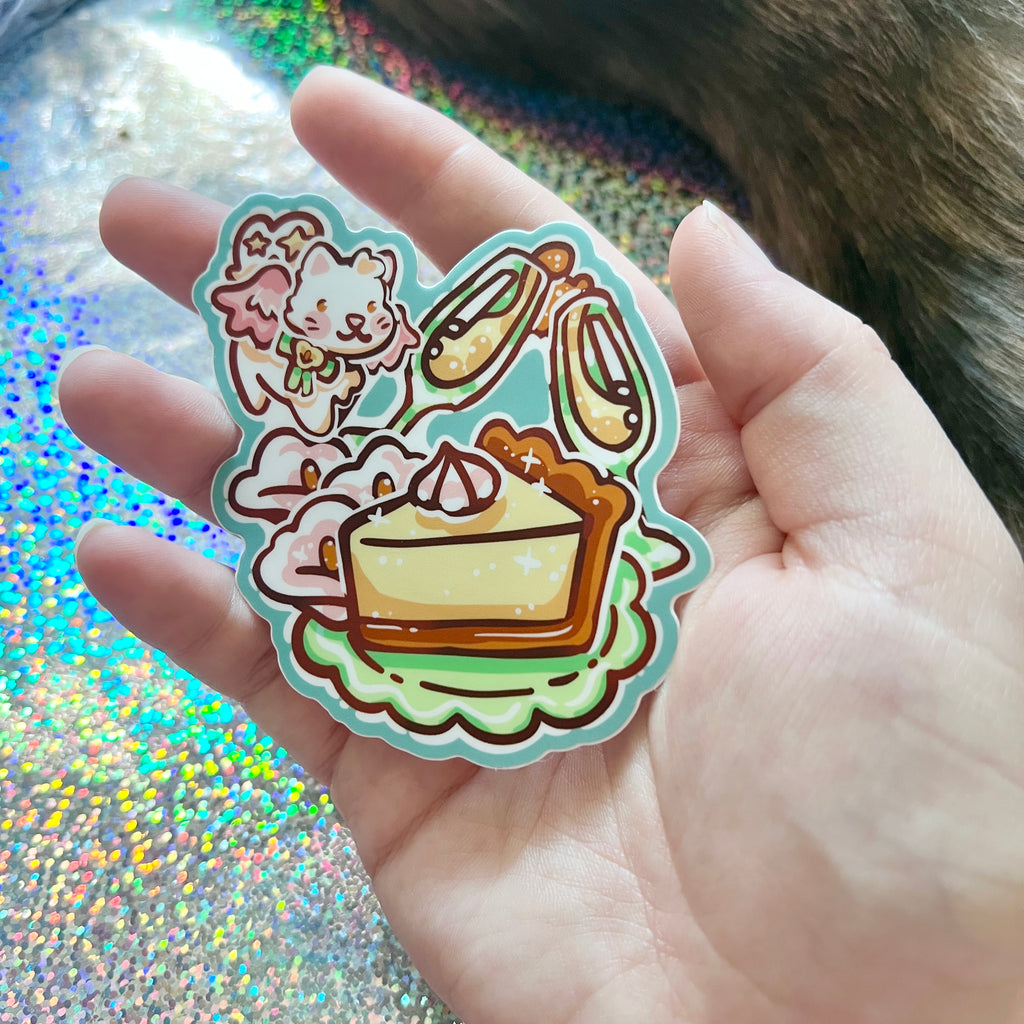 Hand holding a Sticker of a white angel cat flying around a celebration meal against a glittery background