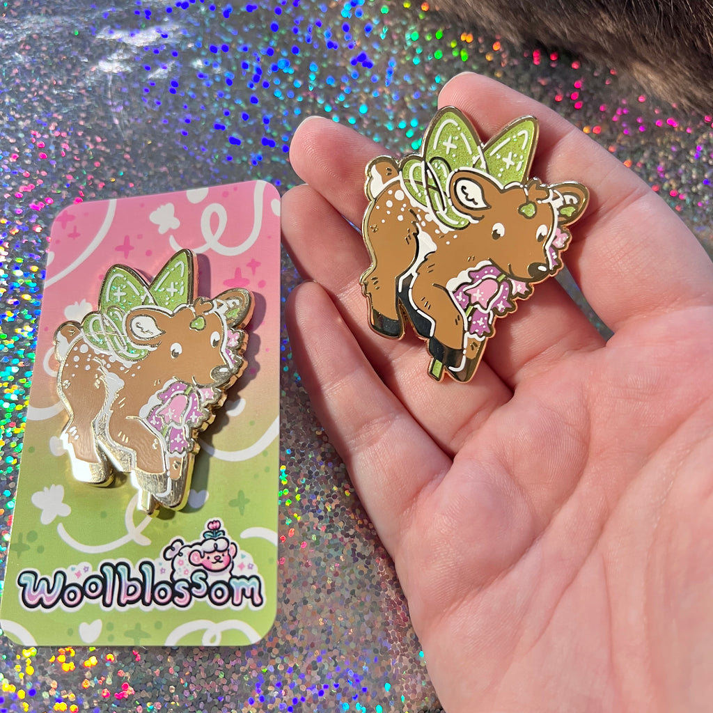 Hand holding a decorative deer pin with a glittery background
