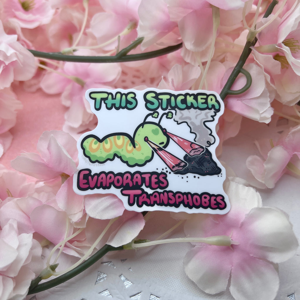 A sticker of a green worm shooting lasers out of its eyes onto a pile of ash with text that says "this sticker evaporates transphobes"