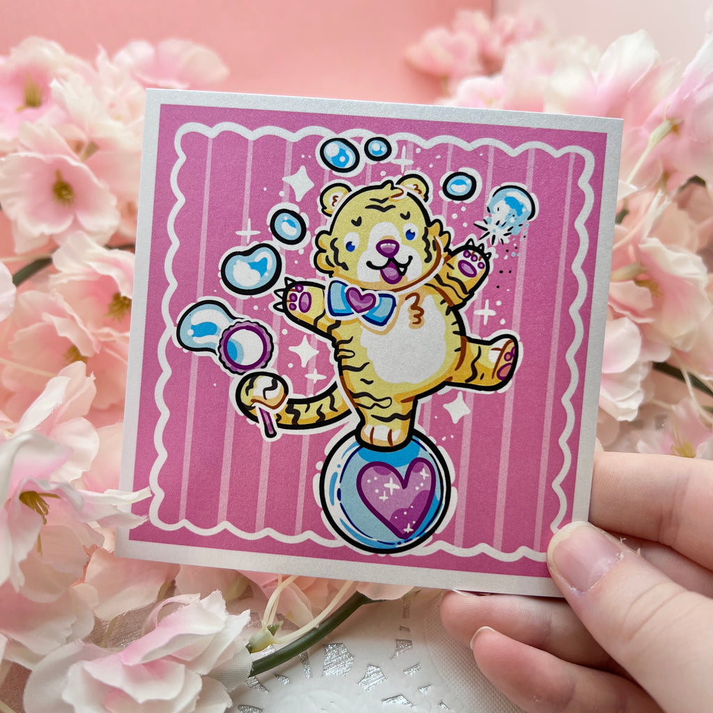 A print of a cute tiger balancing on a ball, bubble wand in tail, reaching up and poking the bubbles with his claws. Pink aesthetic overall.