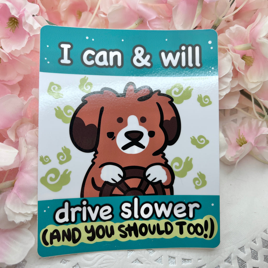 a bumper sticker of a dog driver with a determined expression and surrounded by tiny snails, with text that says "i can and will drive slower (and you should too!)"