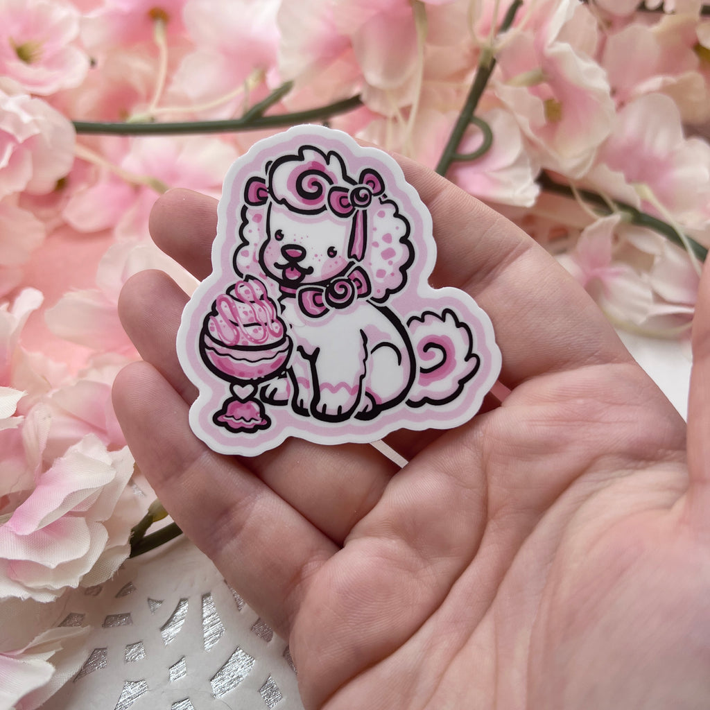 A sticker of a white puppy with pink accents and bows eating ice cream