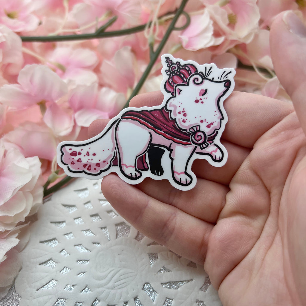 A sticker of a white fox with red specks, red robe, and red peppermint crown