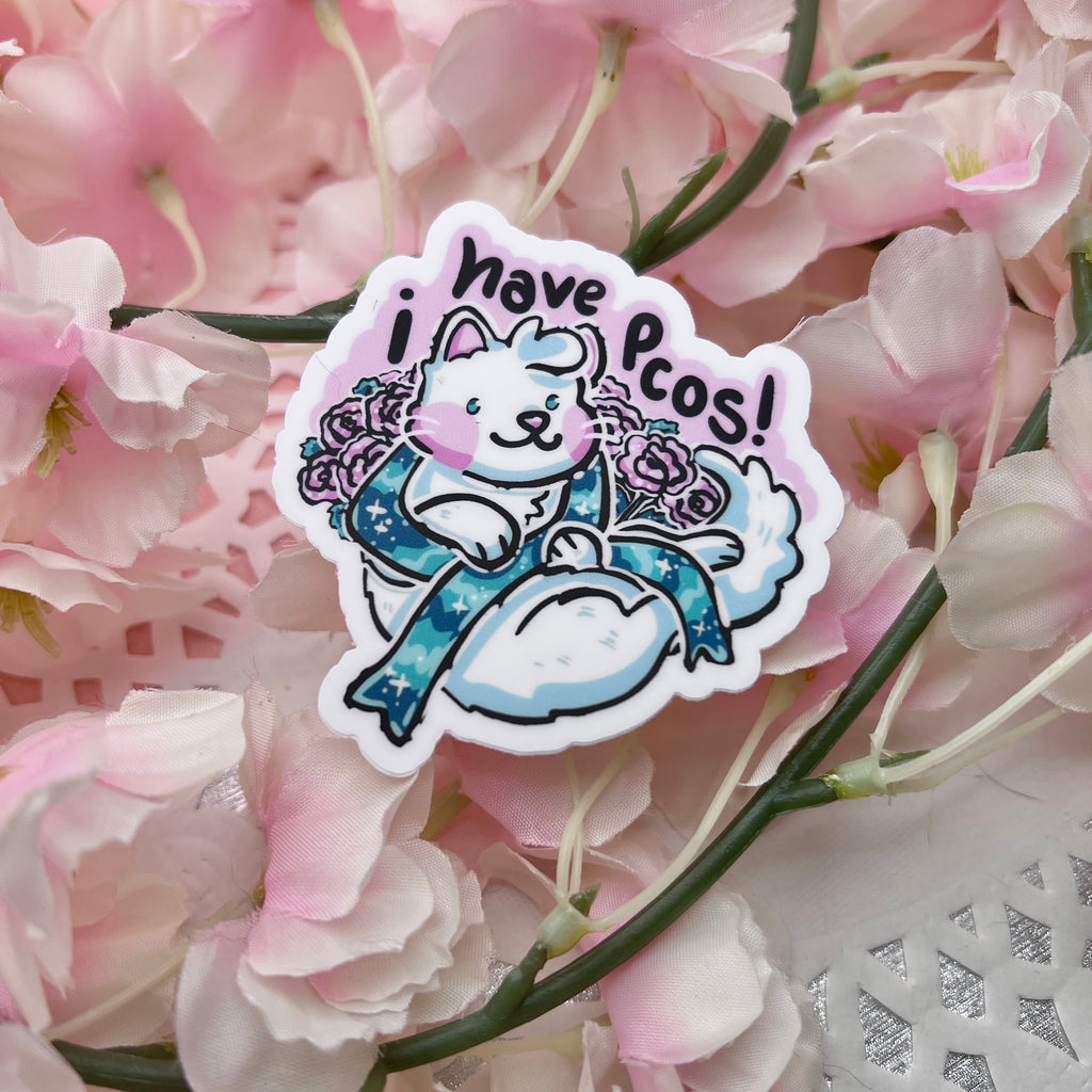 a sticker of a white cat surrounded by pink carnations. the cat is holding a teal condition ribbon and above them is the text "i have pcos"