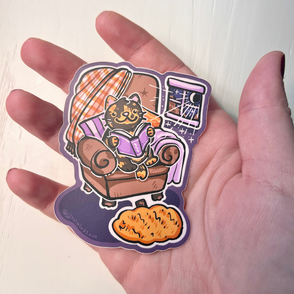 Sticker of a cat reading in a chair on a hand on a white background held by a hand