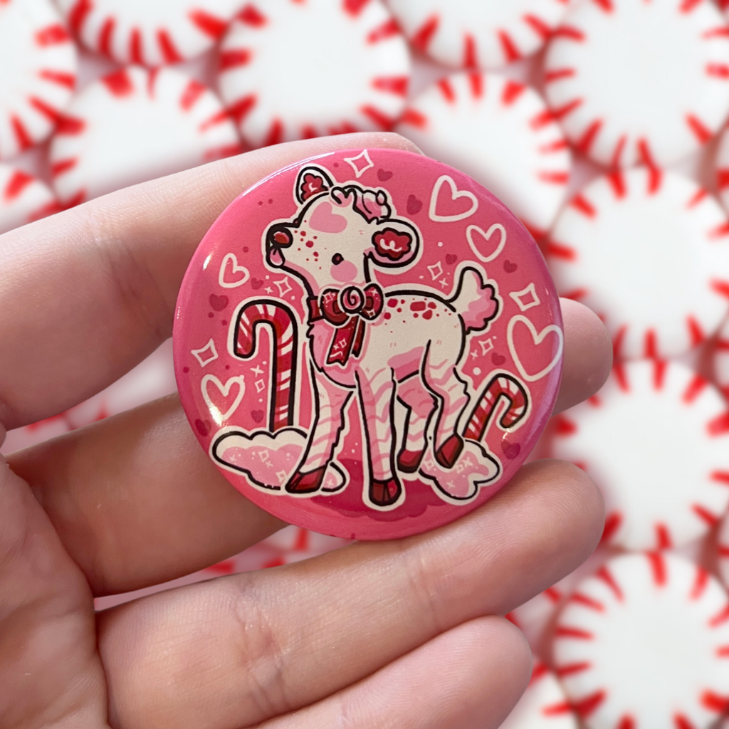 A button of a white deer that has pink and red accents and is peppermint themed