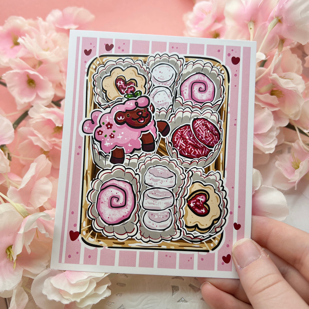 A print of tulip the sheep laying in a box of cookies, with a pink valentines theme