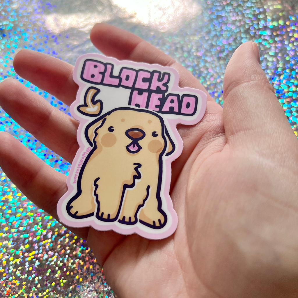Hand holding a sticker with a cartoon dog and 'Block Head' text against a glittery background