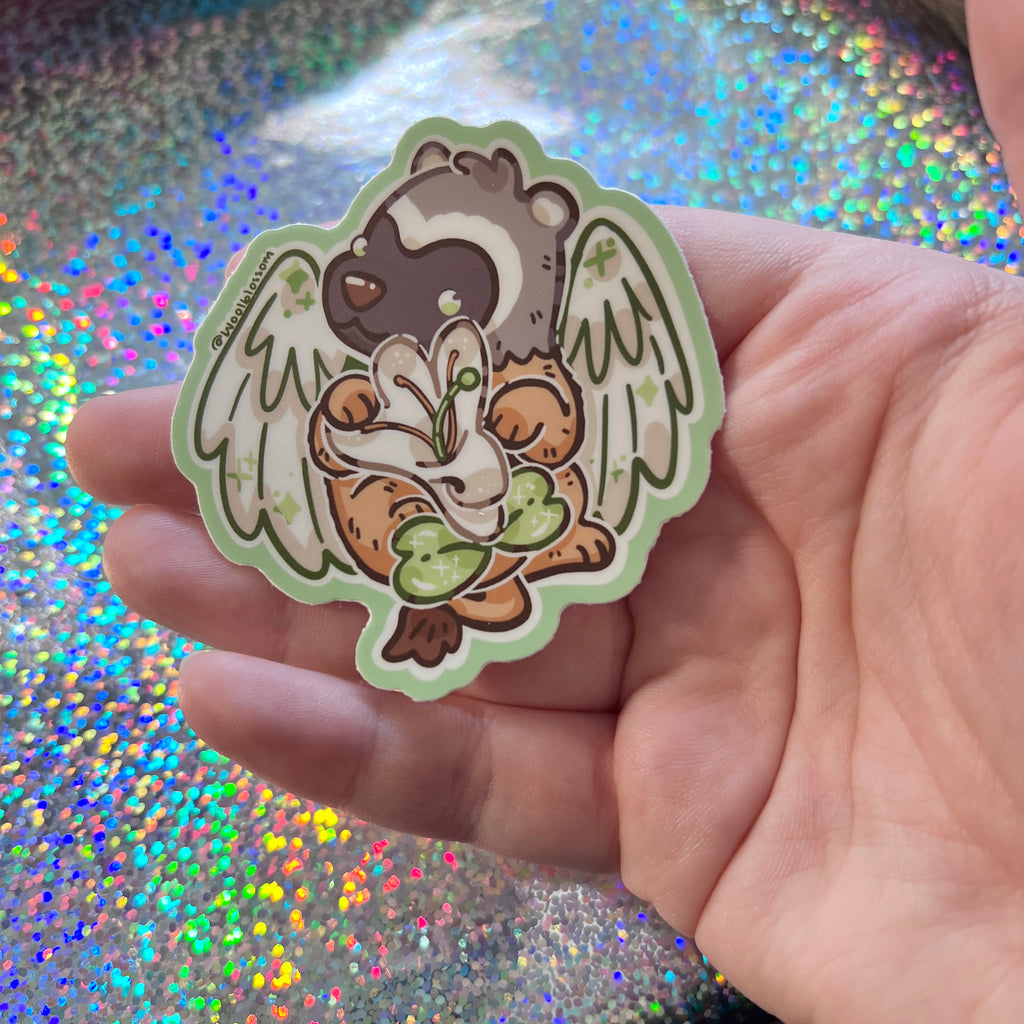 Hand holding a sticker of a badger gryffin holding a honeysuckle against a glittery background