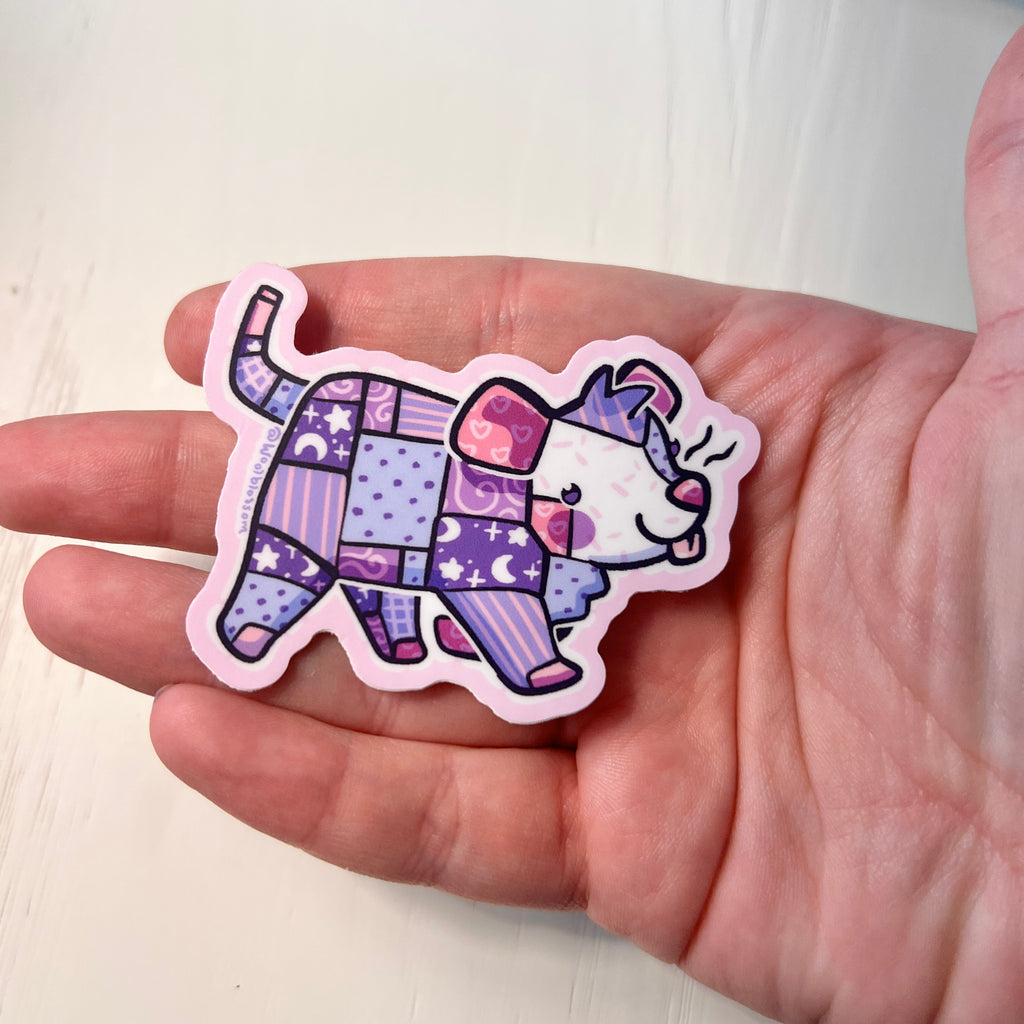 Sticker of a colorful patchwork opossum design held by a hand