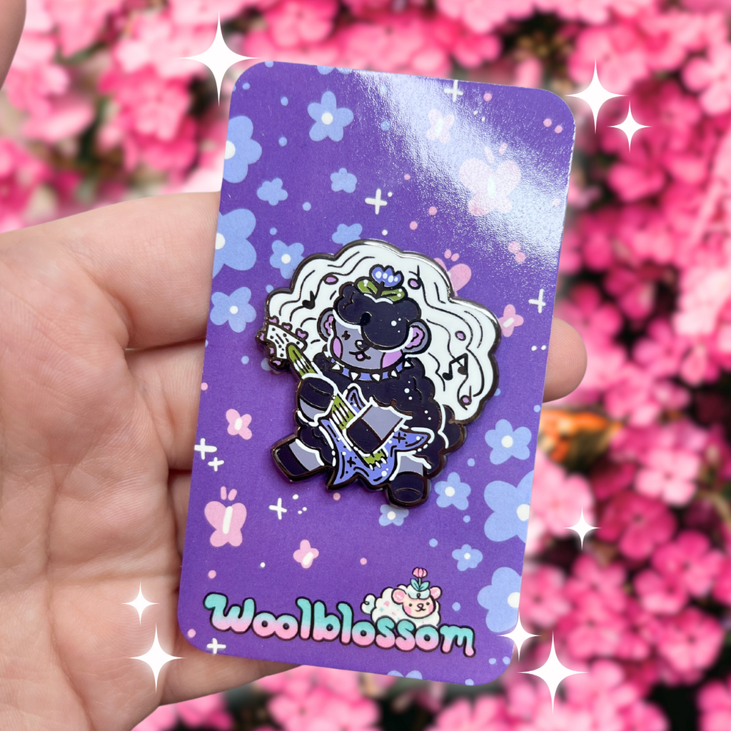 An enamel pin of Violet, the purple colored sheep, strumming on her tulip shaped electric guitar, with a music staff and notes behind