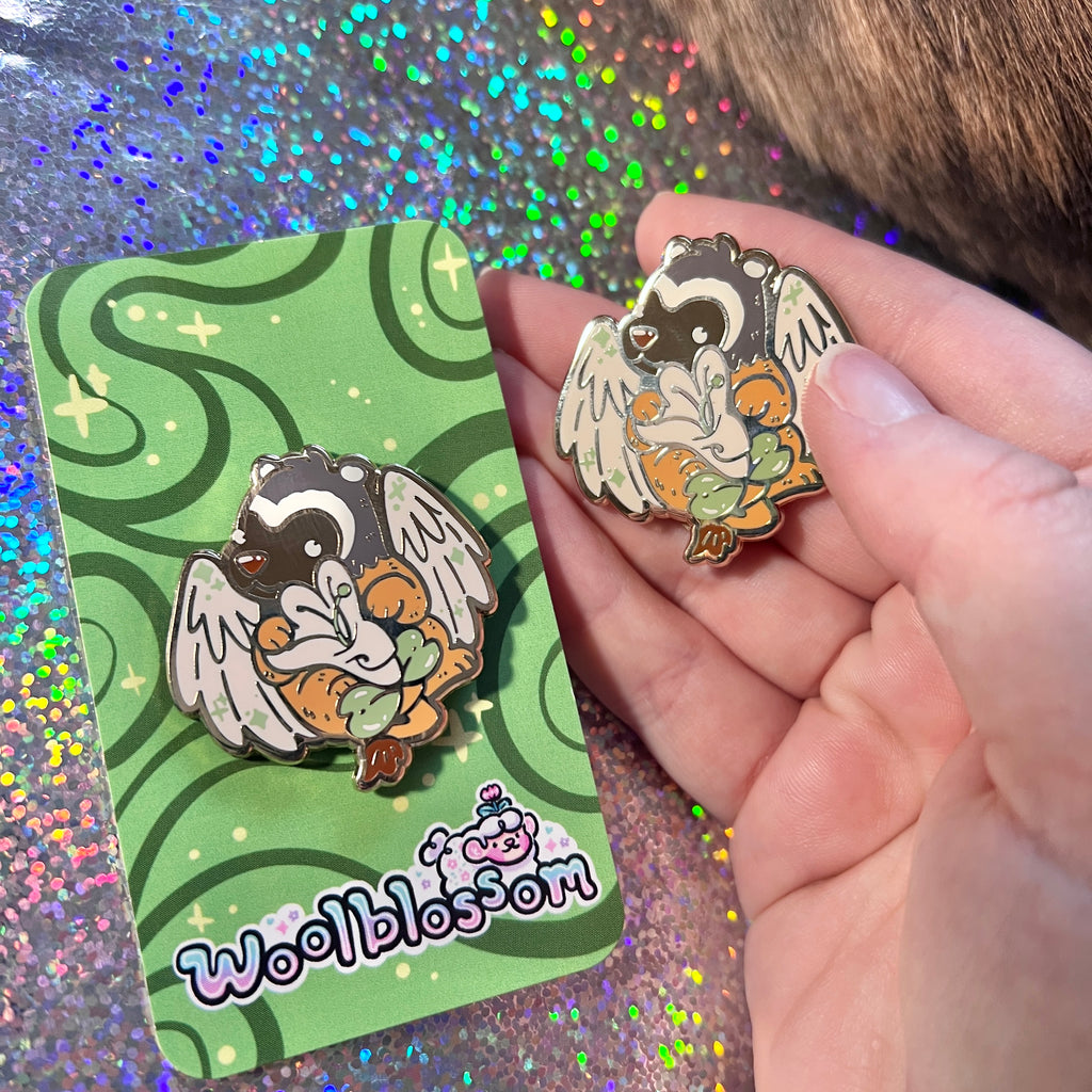 an enamel pin of a badger gryffin holding a honeysuckle  held by a hand next to its packaging on a glittery background