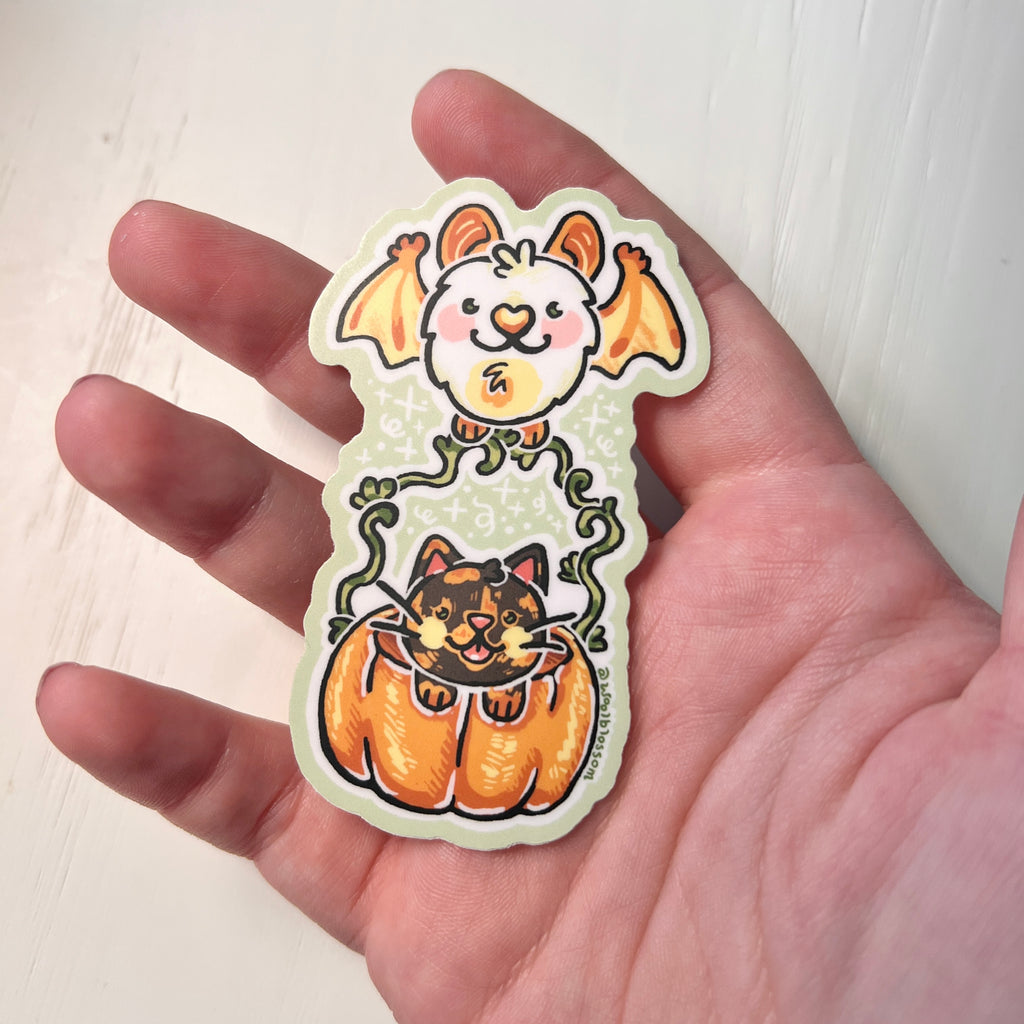 Halloween-themed sticker with a cat in a pumpkin and bat held by hands against a white background held by hand