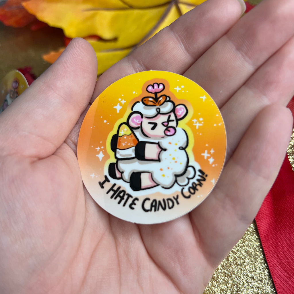 A sticker of a sheep holding a candy corn, sticking its tongue out, with the text "I hate candy corn!"