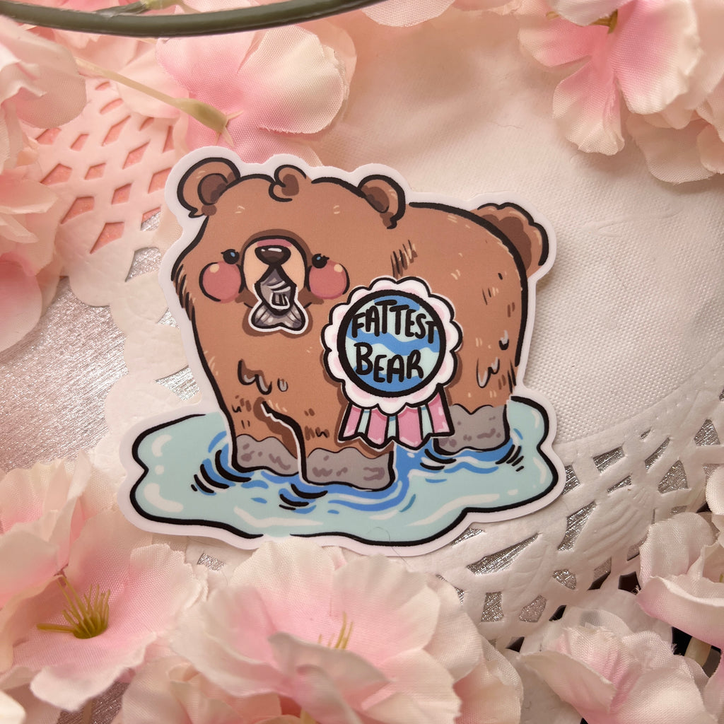 A sticker of a bear in water /w a fish in its mouth and a medallion that says "fattest bear"