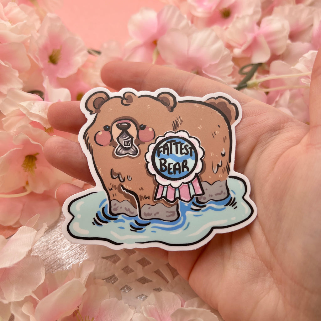 A sticker of a bear in water /w a fish in its mouth and a medallion that says "fattest bear"