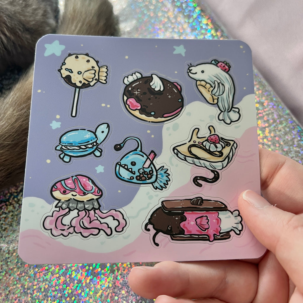 Cartoon stickers of food item sea creatures on a colorful sticker sheet held by a hand.