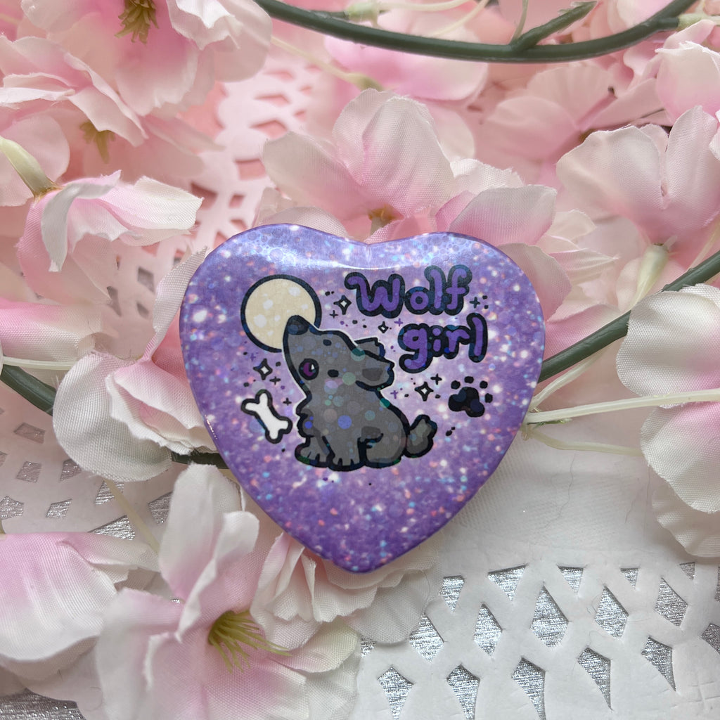 a heart button that says wolf girl with a grey wolf howling in front of a moon, the background of the button is purple glitter