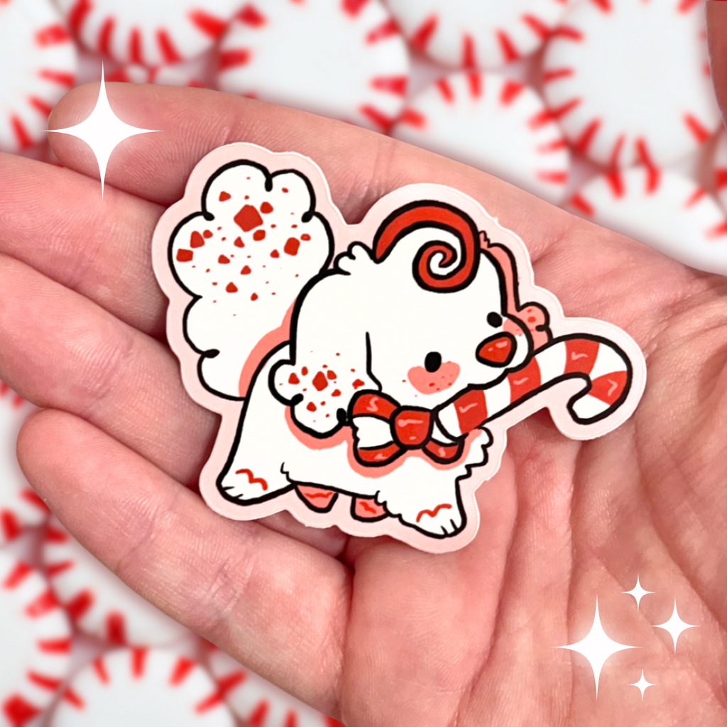 A sticker of a white peppermint bark themed puppy holding a candy cane in her mouth